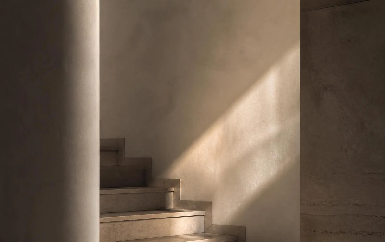Stone stair treads and a plaster wall crossed by a soft shaft of light
