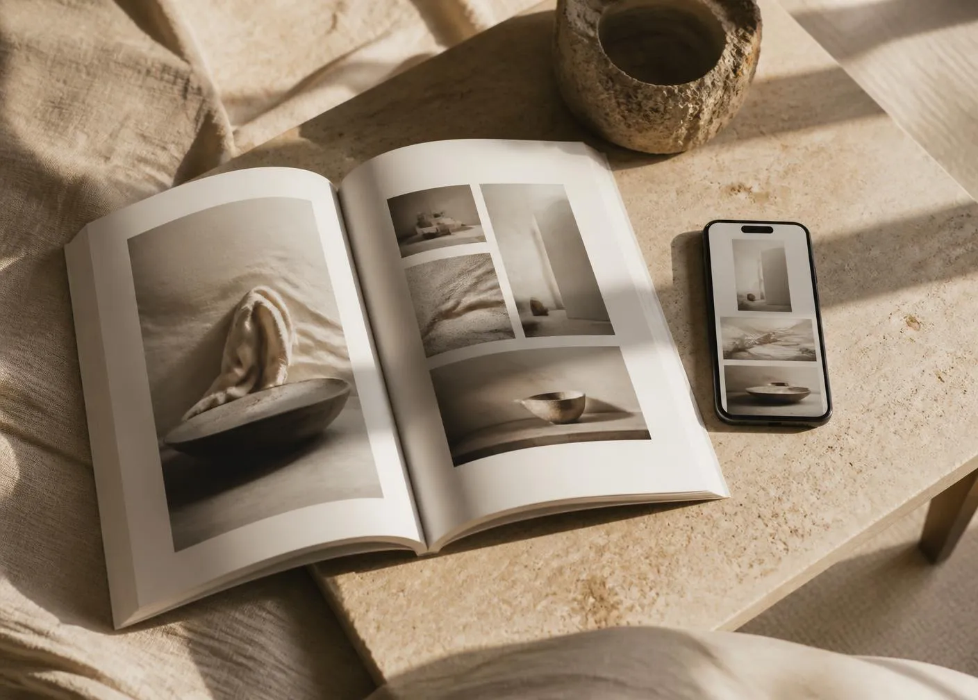 An open editorial magazine and a phone showing a minimal creator portfolio on a travertine table in warm light